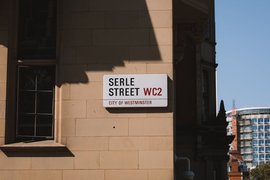 Close-up of a beige stone wall featuring a white and red sign displaying 'BELL YARD WC2' with the text 'CITY OF WESTMINSTER' underneath, and a smaller yellow sign warning about 24-hour CCTV surveillance and prosecution of flytippers, alongside a security camera and a white street lamp with a rounded opaque globe, with a clear blue sky in the background. The area appears clean and well-maintained, with no visible dust or debris, and the lighting suggests daylight conditions. The image captures the urban residential or commercial environment associated with Westminster Council regulations, aligning with surface cleaning and maintenance themes relevant to Pimlico.